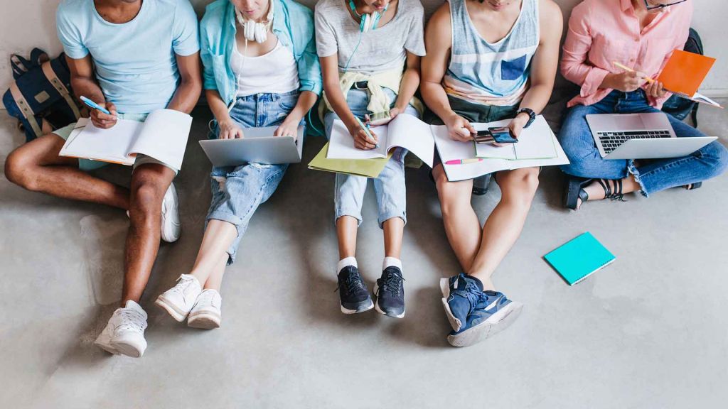 Cames d'alumnes asseguts a terra amb llibretes i portàtils